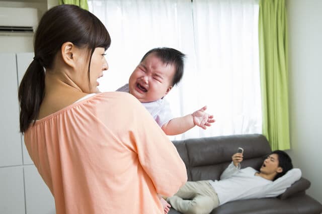 泣く赤ちゃんをあやすママと無関心のパパ